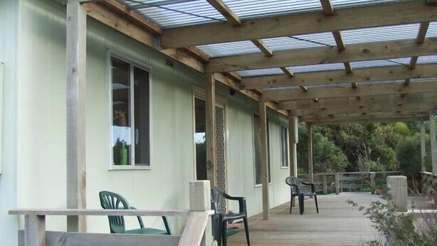 A covered porch with wooden railings, a green chair, and a bench.