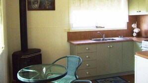 A compact kitchen with a single sink, a window with a curtain, a small dining table with a chair, and a black stove.