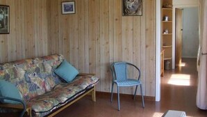 A room with a wooden paneled wall, a sofa with a floral cover, a metal chair, and a door leading to another room.