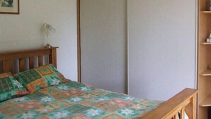 A bedroom with a bed, a bedside table, a lamp, a wardrobe, and a shelf with items.