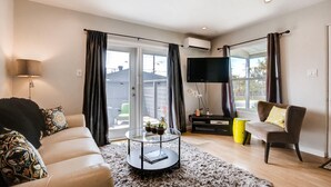 A living room with a sofa, armchair, coffee table, TV, and a balcony with curtains. - Tranquil Hip Indoor/Oudoor Living. Just Blocks from Sand. (Oceanside)