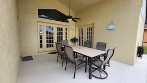 Eine überdachte Terrasse mit Tisch und Stühlen, einem Deckenventilator und einer Wanduhr.