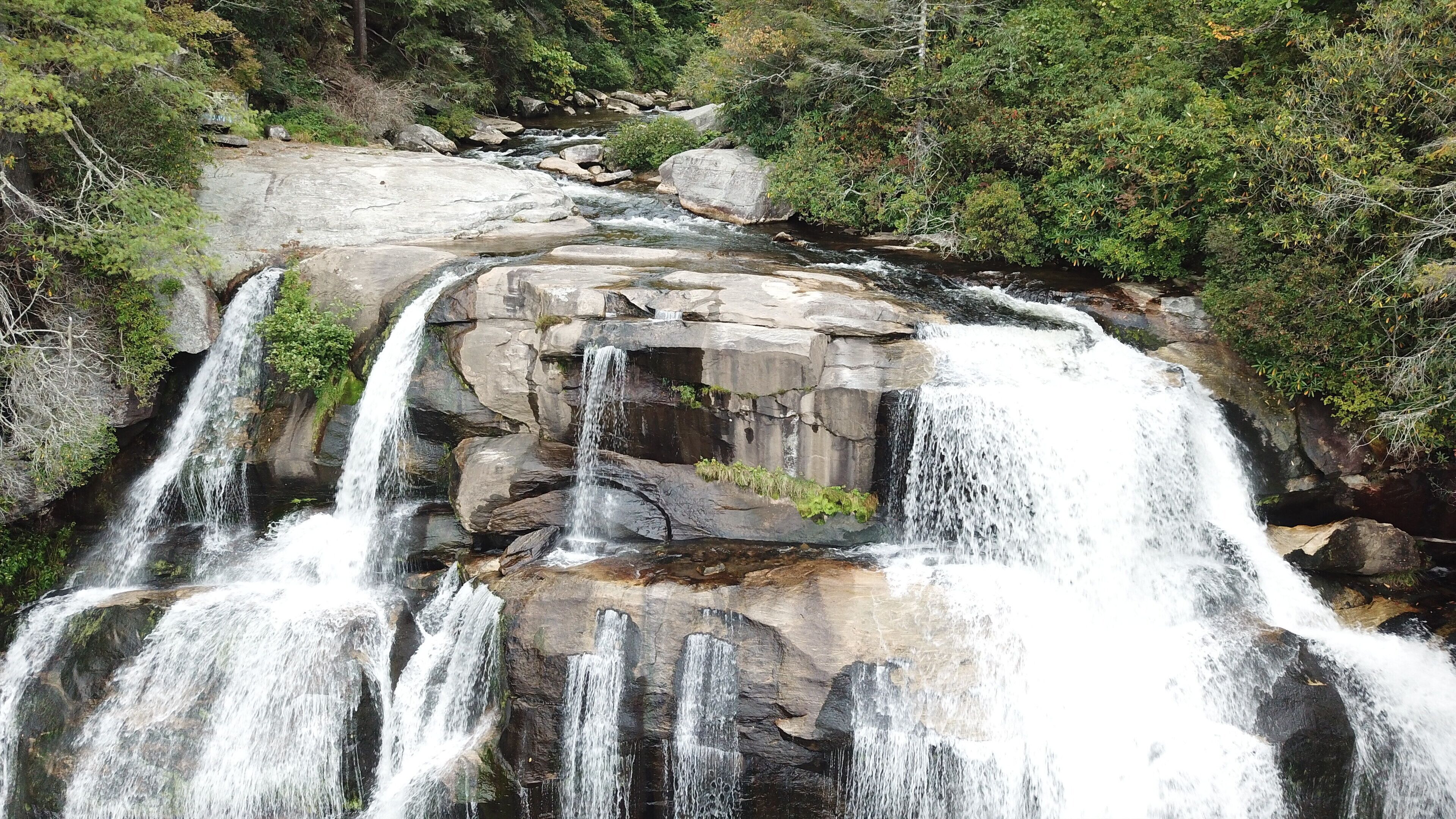 Une cascade d’eau se déversant sur de gros rochers, le tout entouré d’une végétation luxuriante.