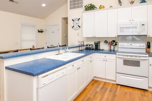 A kitchen with white cabinets, a blue countertop, a white dishwasher, a stove, and a clock on the wall. - Gone Coastal - 2nd Row home; 4BR; Ocean Views from Sun Deck (Surf City)