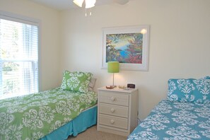 A bedroom with two beds, a nightstand, a lamp, a framed picture, and a window with blinds.