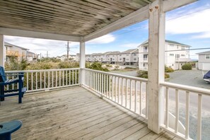 A covered porch with a view of a residential area, featuring a wooden floor and white railings.