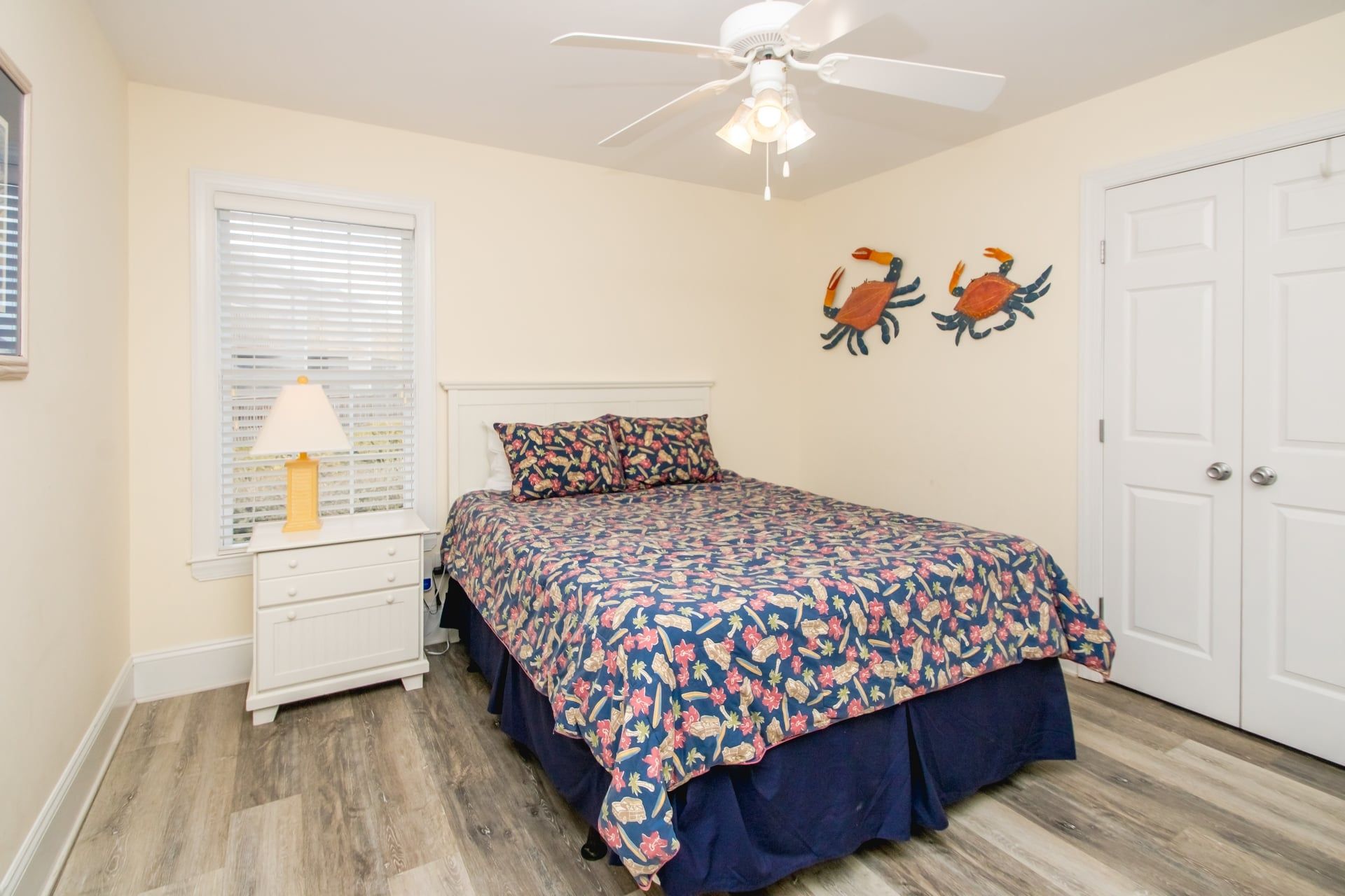 A bedroom with a bed, a nightstand, a lamp, a ceiling fan, and two wall art pieces.