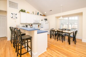 A kitchen with a central island, bar stools, a dining table with chairs, and a window with blinds. - Gone Coastal - 2nd Row home; 4BR; Ocean Views from Sun Deck (Surf City)