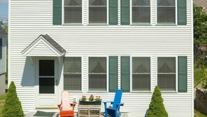 A two-story white house with green shutters, a front porch with a bench, and a picnic table in the front yard. - Goose Rocks Cottage at One Long Beach (York Beach)