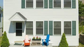 A two-story white house with green shutters, a front porch with a bench, and a picnic table in the front yard.