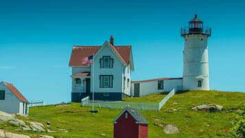 A lighthouse with a white exterior and a red roof, a white house with a red roof, and a small red shed.