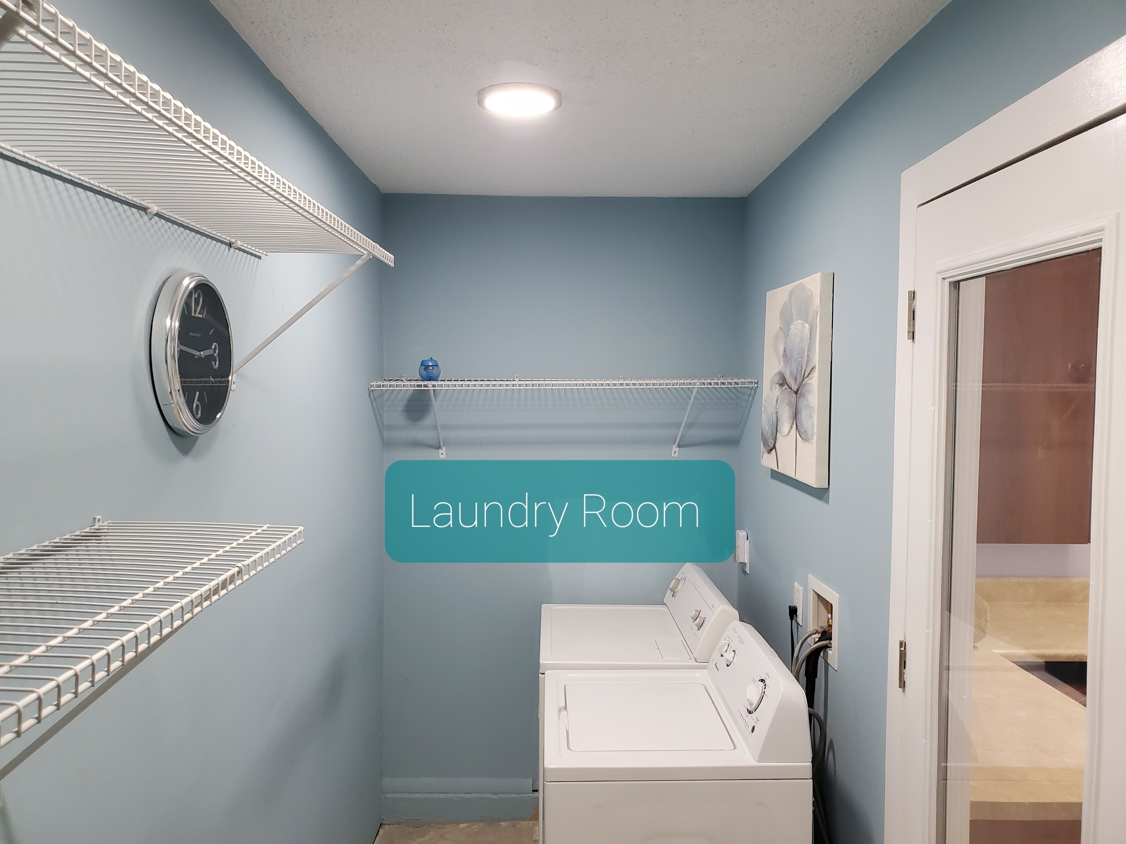 A laundry room with a washing machine, drying racks, and a clock on the wall.