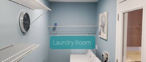 A laundry room with a washing machine, drying racks, and a clock on the wall.