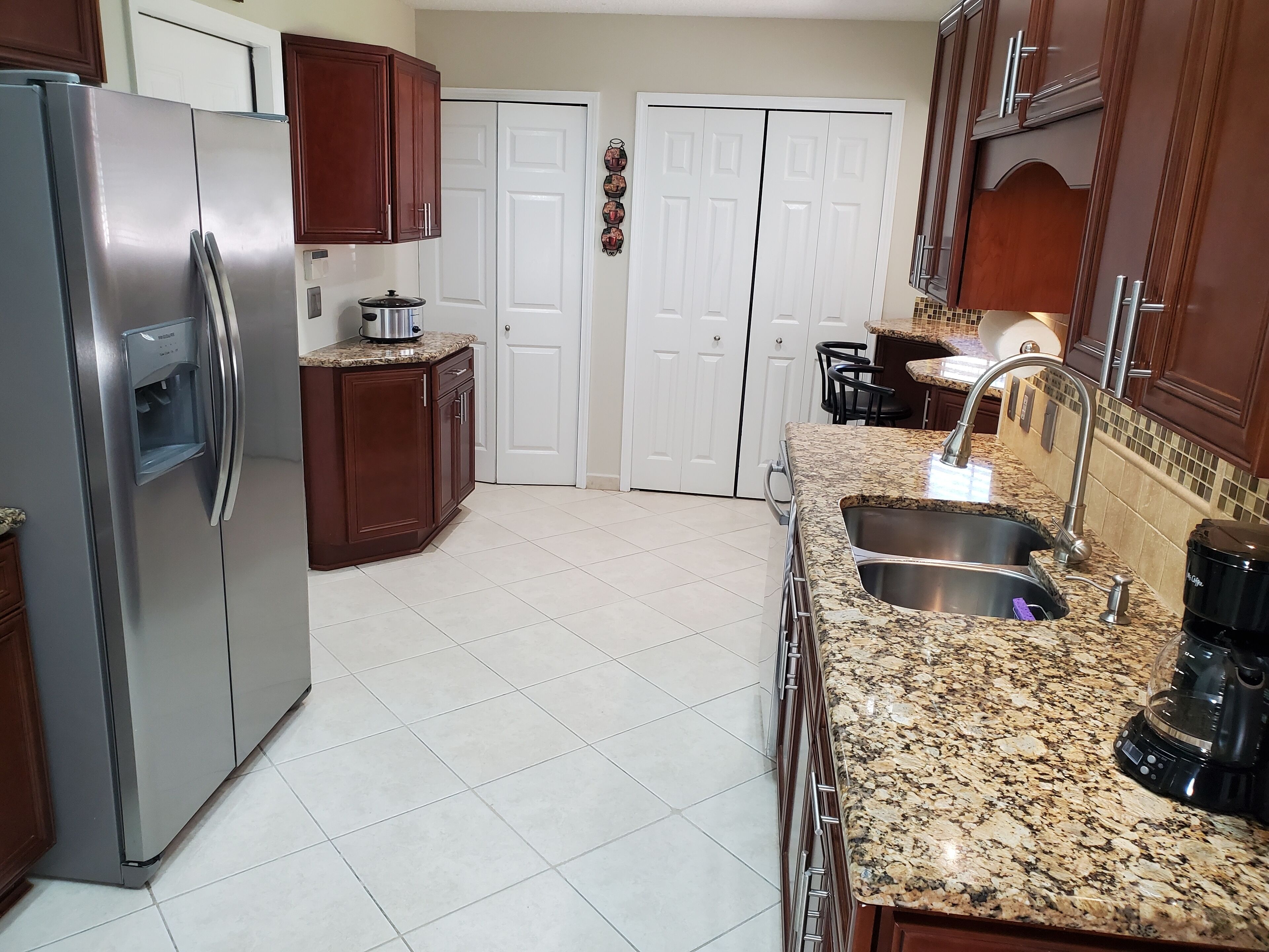 A kitchen with a stainless steel refrigerator, granite countertops, a double sink, and wooden cabinets.