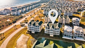 An aerial view of a coastal residential area with multiple apartment buildings, a beach, and a prominent location marker. - Cottagevacations4u "Island Dunes" Villa ocean view- elevator- pool club-pickleball-tennis (Ocean Isle Beach)