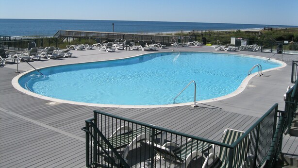 A pool with lounge chairs and a view of the ocean. - Cottagevacations4u "Island Dunes" Villa ocean view- elevator- pool club-pickleball-tennis (Ocean Isle Beach)