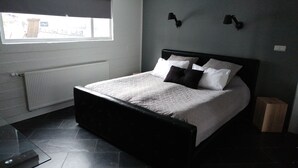A bedroom with a bed, a window, a radiator, and a wall-mounted lamp.