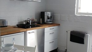 A compact kitchen with white cabinets, a wooden countertop, a built-in stove, a coffee maker, and a window providing natural light.