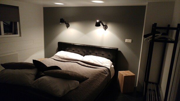 A bedroom with a bed, two wall-mounted lamps, a radiator, and a wooden nightstand.