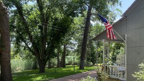 Eine überdachte Veranda mit einer amerikanischen Flagge, umgeben von Bäumen und einem Schotterweg.
