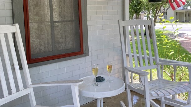 Eine Veranda mit weißen Schaukelstühlen und einem kleinen Tisch mit zwei Sektgläsern.