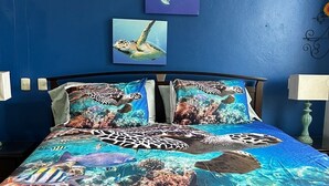 Un letto con copriletto a tema oceano, due quadri a parete raffiguranti tartarughe marine e una ventola a soffitto.