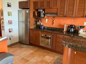 A kitchen with wooden cabinets, a stainless steel refrigerator, a microwave, a stove, and a coffee maker.