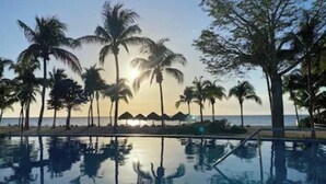 Vista libera su una piscina, palme e un tramonto sullo sfondo.