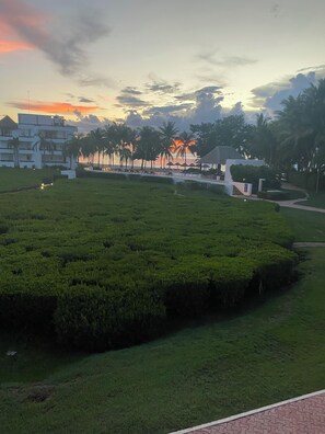 A landscaped area with a pool, palm trees, and a building with multiple balconies. - A Beachfront Condo in Paradise with Breathtaking Views! Heated Pools & WIFI!! (Cozumel)