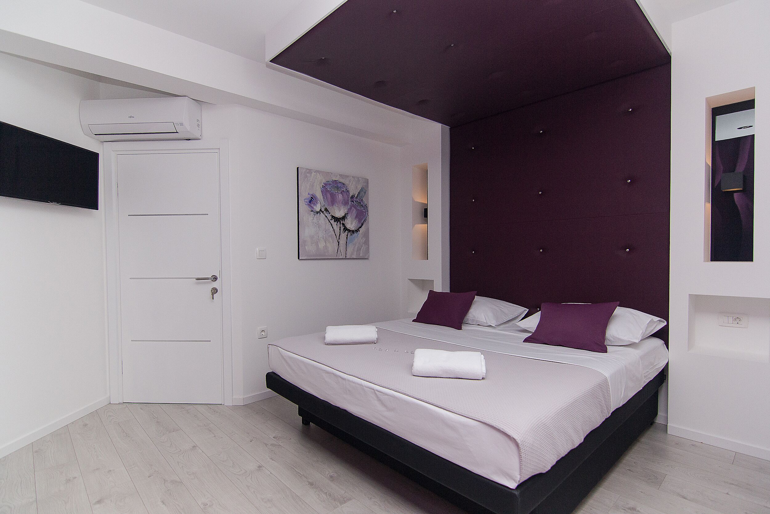 Una camera da letto moderna con un letto, una porta, un condizionatore d'aria e un'opera d'arte appesa al muro.