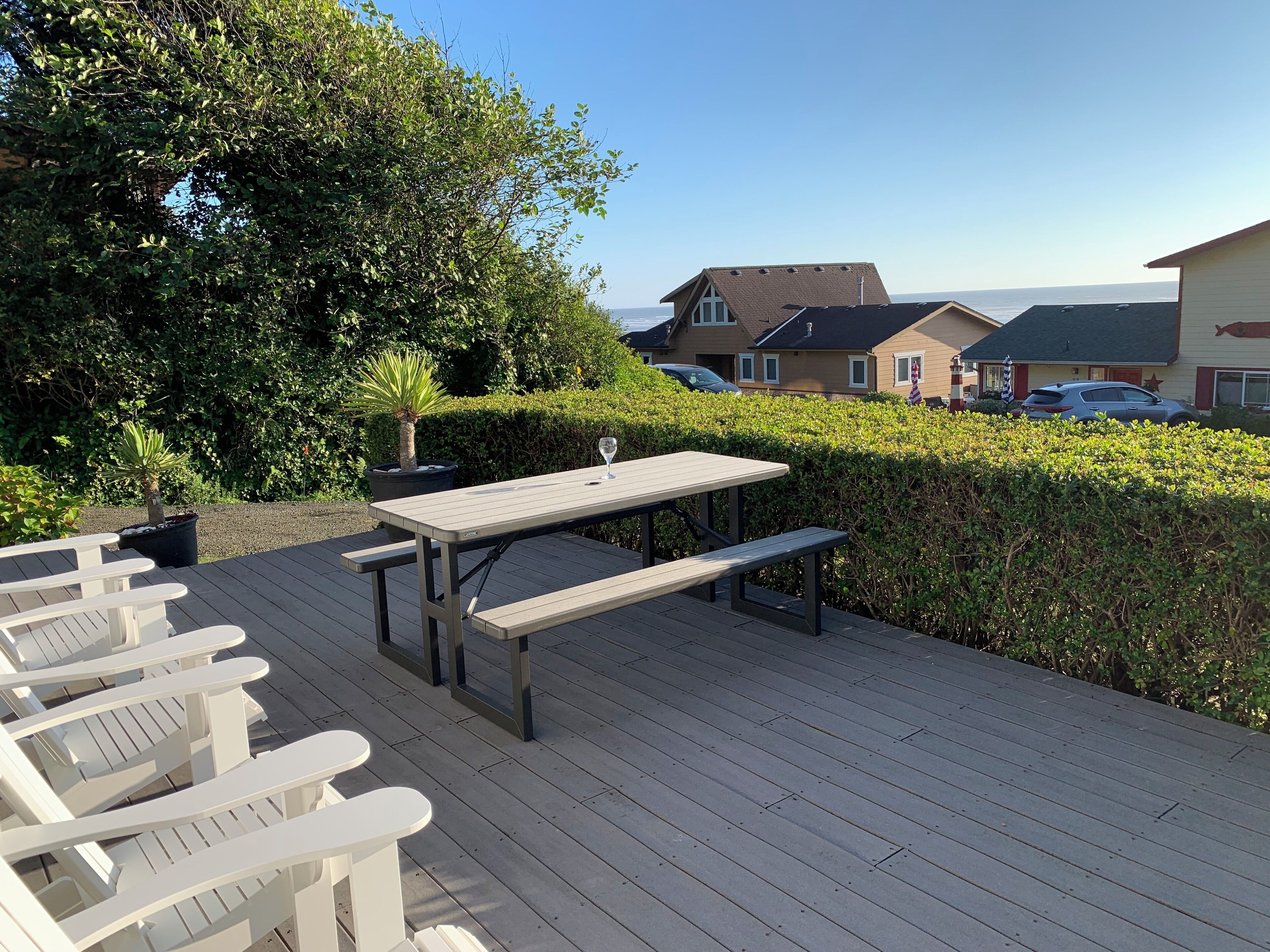 A wooden deck with picnic tables and benches, surrounded by greenery and overlooking a residential area.