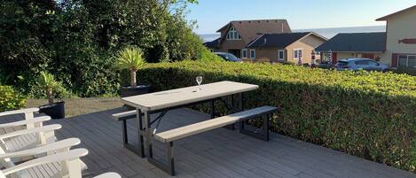 A wooden deck with picnic tables and benches, surrounded by greenery and overlooking a residential area.