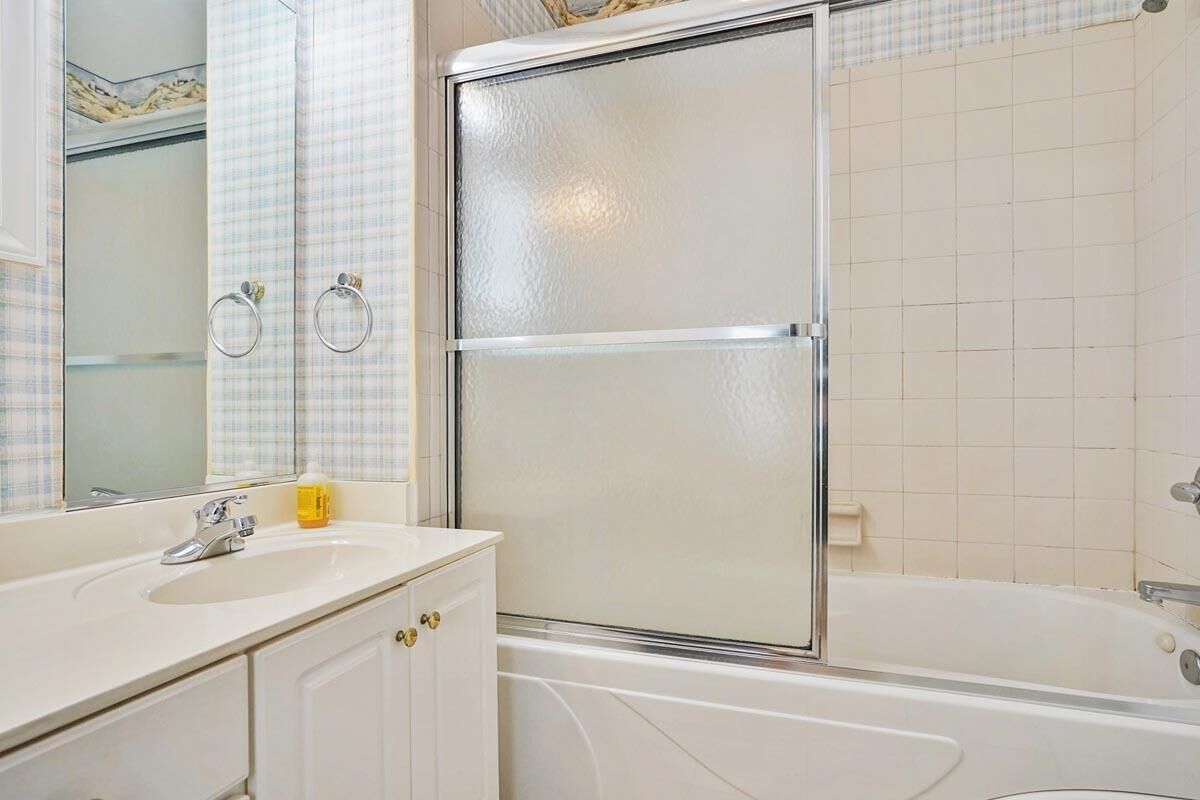 Une salle de bain avec un lavabo blanc, un miroir, une douche en verre et une baignoire.