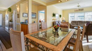 A spacious living area with a glass-top dining table, comfortable seating, and a view of the outside. - CottageVacations4u "BEACH HAVEN"  ocean view-pool club-direct access to beach-dog friendly (Ocean Isle Beach)