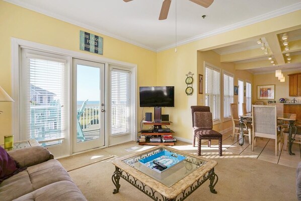 A living room with a sofa, coffee table, TV, and a dining area with chairs and a table. - CottageVacations4u "BEACH HAVEN" ocean view-pool club-direct access to beach-dog friendly (Ocean Isle Beach)