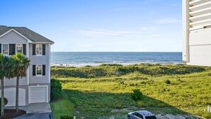 A two-story house with a garage, a lawn, and a view of the ocean. - CottageVacations4u "BEACH HAVEN"  ocean view-pool club-direct access to beach-dog friendly (Ocean Isle Beach)
