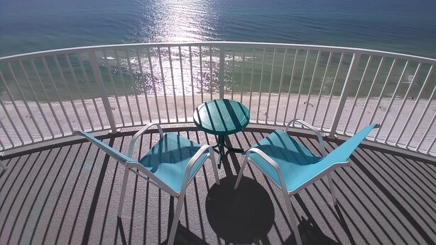 Un balcon avec une table et deux chaises, donnant sur une plage et l’océan.