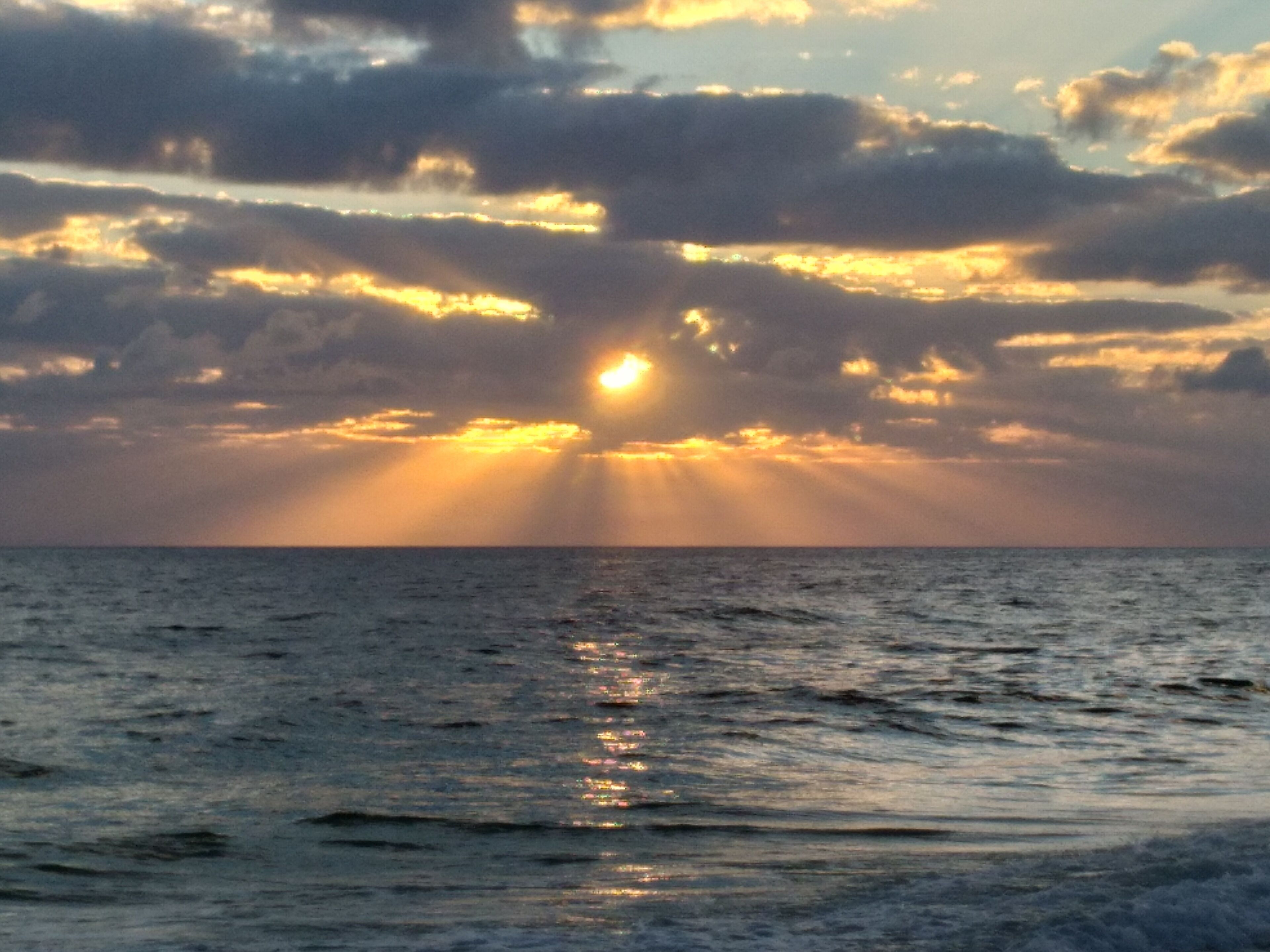 Un coucher de soleil sur l’océan, les nuages reflétant la lumière du soleil.