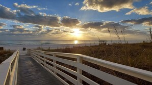 Une promenade en bois menant à une plage, avec un coucher de soleil en arrière-plan.