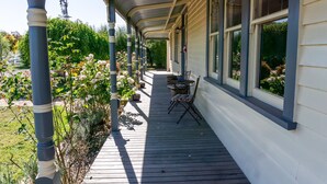 A covered wooden deck with a table and chairs, surrounded by potted plants and flowers.