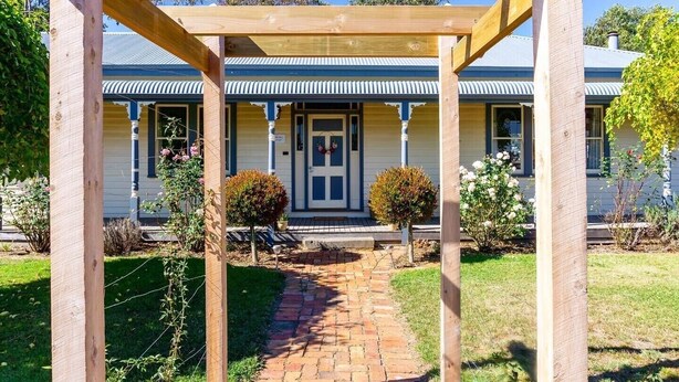 A wooden pergola structure in front of a house with a brick pathway leading to the entrance.