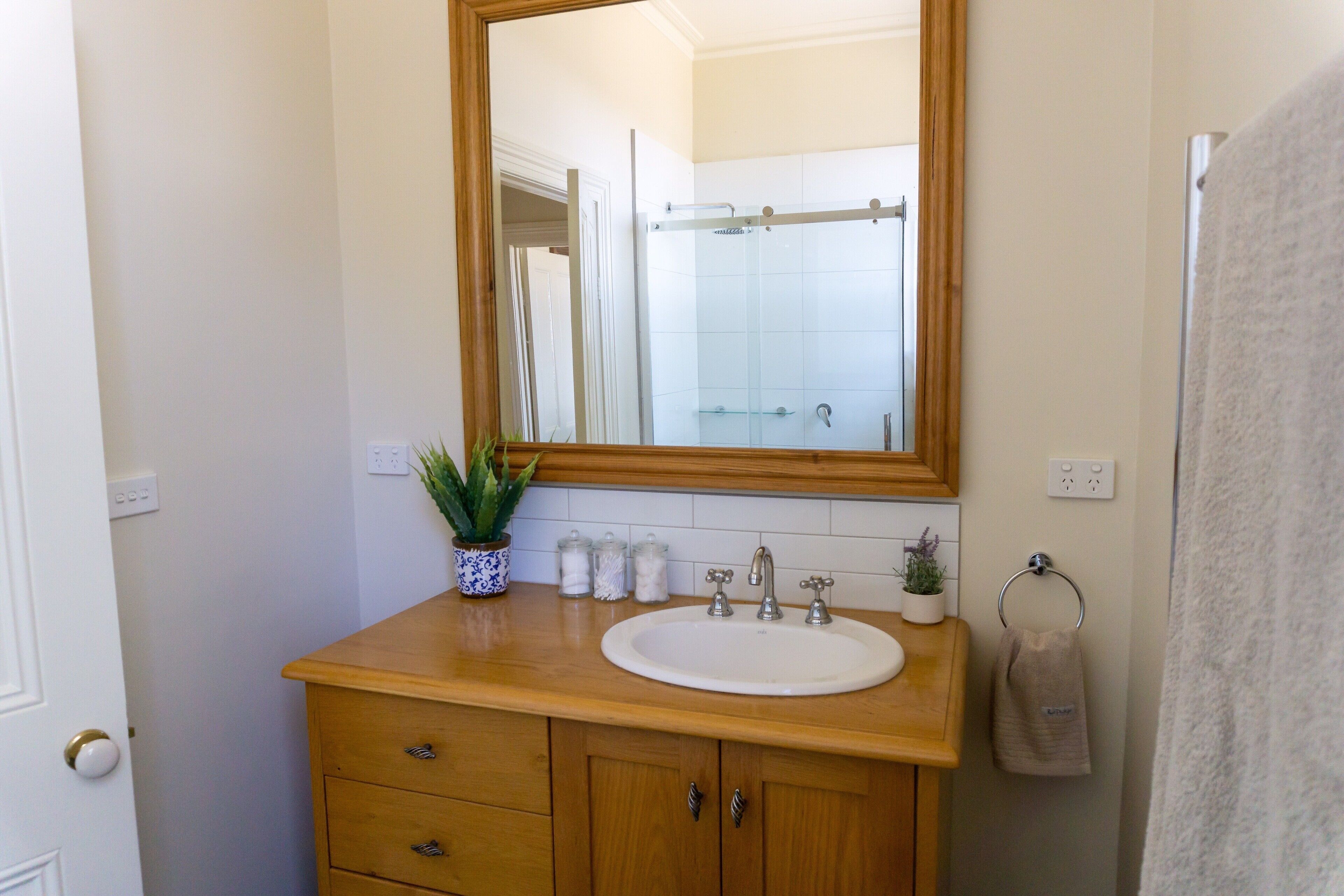 A bathroom with a wooden vanity, a white sink, a mirror, and a towel rack.