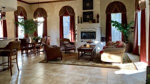 Amplia sala de estar con chimenea, muebles de cuero y ventanas grandes con cortinas.