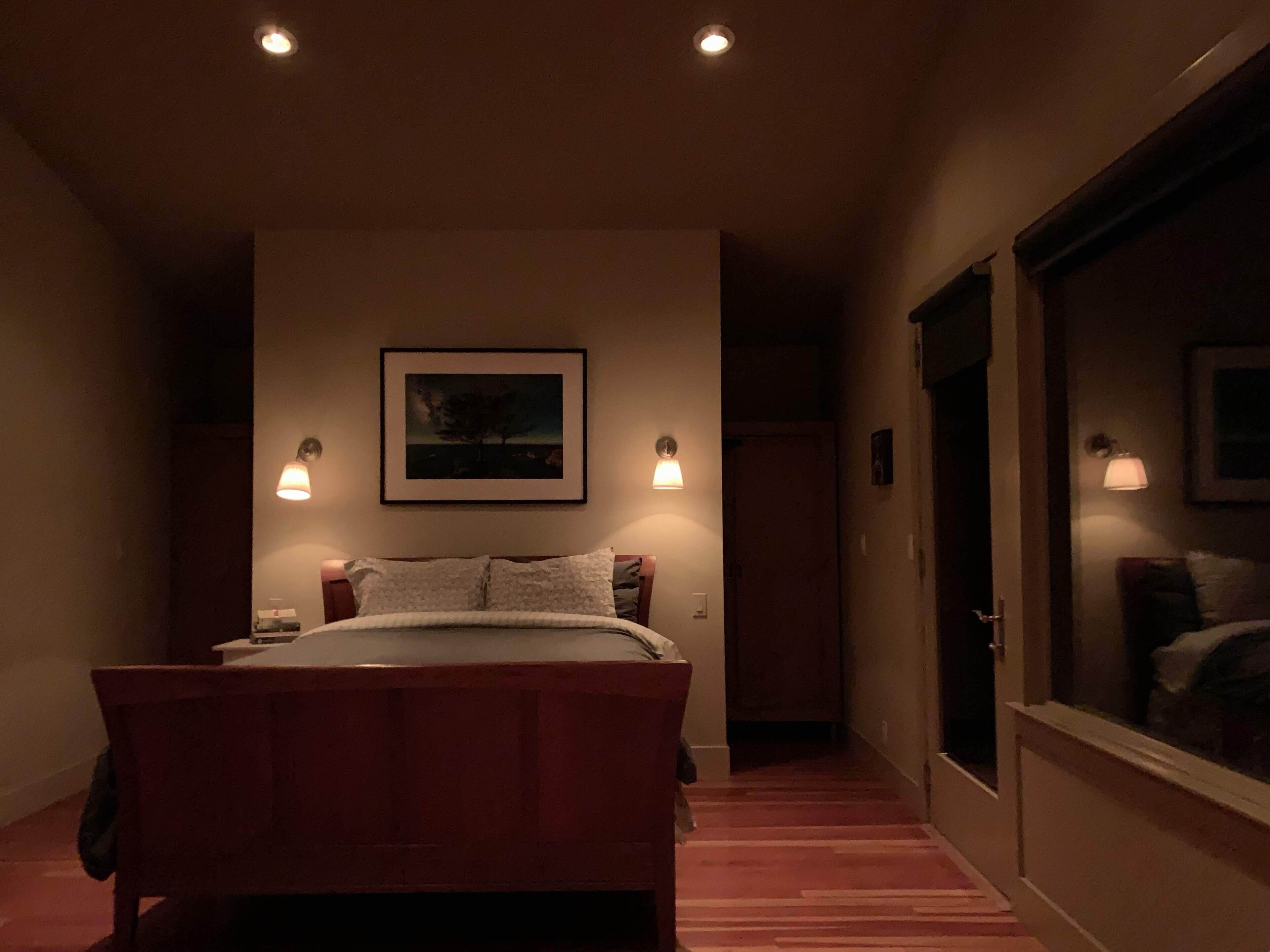 Un dormitorio con una cama, dos lámparas de noche, un cuadro enmarcado en la pared y una ventana con vistas.