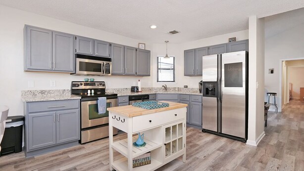 A modern kitchen with grey cabinets, stainless steel appliances, and a wooden island.