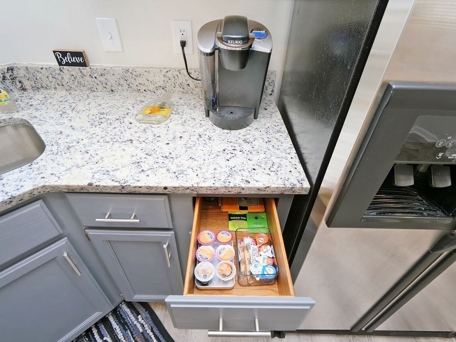 A kitchenette with a coffee maker, a drawer with tea bags, and a 'Believe' sign on the wall.