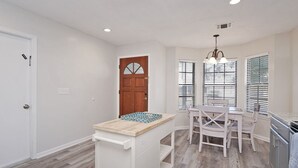 A kitchen with a wooden island, white cabinets, and a dining area with chairs.