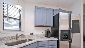 A kitchen with granite countertops, a stainless steel refrigerator, and grey cabinets.