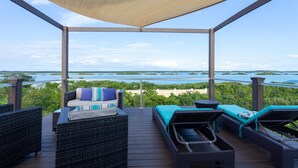 A covered outdoor deck with wicker furniture, a bed, and a view of the water. - Escape to Exhale at a modern style villa with breathtaking views of chalk sound (Providenciales)