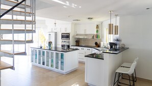 A modern kitchen with white cabinetry, a central island, and a staircase leading to an upper level. - Escape to Exhale at a modern style villa with breathtaking views of chalk sound (Providenciales)